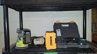 Overview of Ryobi sander, yellow DeWalt bit case, assembled black hard case with Ryobi drill inside, and two metal crow bars on a black metal table.