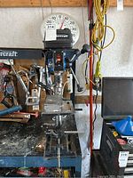 Front view of the MasterCraft drill press on a workbench, showing the head assembly and chuck with drill bit attached.
