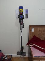 Full view of vacuum mounted on wall bracket next to bed and books