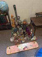 Group of figurines, wall hangings, vases, candleholders, and plaques arranged on carpeted floor near bookshelf and table