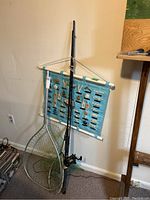 Fishing rod and two fishing nets leaning against a wall, with a blue wall hanging showing knots hung behind them