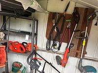 Photo showing black and red Black and Decker hedge trimmers, trimmers hanging on wall-mounted wooden rack and nearby metal shelving with other tools and extension cord