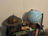 Overall view of two globes and compass on a shelf with books, showing sizes and condition.