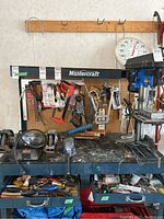 Workbench with various hanging tools including saws, hammer, and drill press at side. Pegboard background shows additional storage and tools.