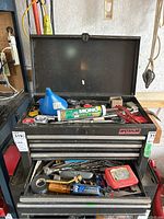 Photo of open black metal tool chest drawers displaying assorted hand tools including screwdrivers, wrenches, socket set, tape measures, and other small hand tools.