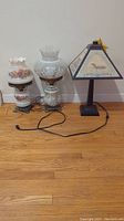 Three electric lamps including two vintage style oil lamps with floral glass shades and one metal lamp with landmark-themed shade