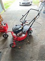 Full view of red Briggs and Stratton mulching lawn mower with black engine cover and folded handlebar, showing three wheels and mower deck.