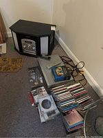 Overall lot view showing the Memorex music station speaker cabinet, Sears DVD player, Lord of the Rings DVD box set, remote, and a pile of CDs.