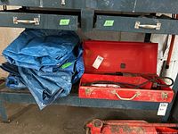 Folded large blue plastic woven tarps stacked next to toolbox, showing general condition and material type.