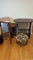 Three small wooden side tables with different shapes and one upholstered foot stool, shown on a hardwood floor against a wall.