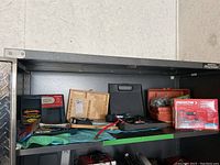 Shelf displaying a variety of tools including black case soldering tool, wooden box chisel set, red tackle box, and an Arrow boxed staple gun kit.