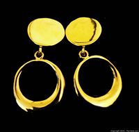 Front view of large vintage gold tone clip-on earrings against black background, showing polished surface and irregular oval shapes.