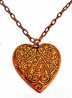 Close-up of the heart-shaped copper pendant showing intricate swirling and floral design details.