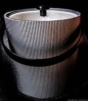Photo showing mid century cylindrical ice bucket with black and white vertical ribs, lid with black knob, and black handle.