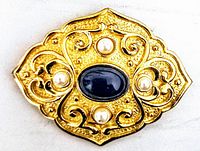 Close-up front view of the vintage gold-tone brooch showing intricate filigree detailing, four round pearls, and central oval dark blue stone.