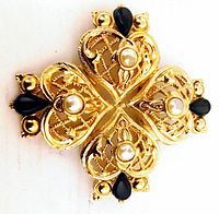 Front view of vintage gold tone brooch showing intricate filigree hearts, each with a central pearl and black teardrop accents.