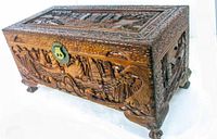 Photo of the vintage wooden chest showing detailed hand carvings of Chinese sailing boats with brass lock hardware on front side.