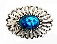Close-up image of vintage brooch showing oval faux turquoise stone with decorative silver-tone openwork frame.