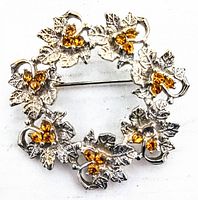 Front view of vintage figural rhinestone wreath brooch showing silver-tone leaves and amber rhinestones.