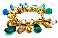 Close-up image of vintage lucite charm bracelet showing gold-tone textured chain links and attached blue and green lucite teardrop charms along with gold-tone seashell charms and faceted clear beads.