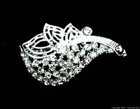 Close-up photo of vintage rhinestone brooch showing leaf-shaped cutout designs and clustered clear rhinestones on front, silver-tone metal.