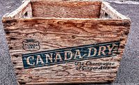 Front view of the wooden crate showing Canada Dry logo and slogan in faded dark blue ink on wood.