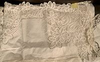 Close-up of fabric showing detailed floral embroidery and lace edge of beige tablecloth or doily