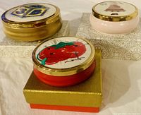 Three round trinket boxes each with unique design on top, displayed on individual presentation boxes.