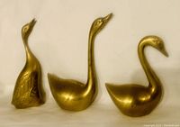 Three vintage brass swan figurines shown standing side by side on a flat surface against a neutral background, highlighting their shape and brass finish.