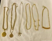 Six ladies necklaces laid out in a row showing variety of chain styles and pendants including a round locket, zodiac pendant, bow pendant, and bar pendant.