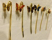 Six gold-plated brass cloisonné enamel bookmarks displayed in a row, featuring butterfly, swan, and elephant designs.