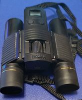 Front view of black Bushnell binoculars showing branded central focus wheel and attached strap.