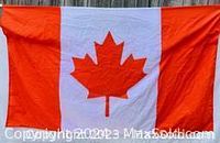 Full view of the Canadian flag showing red maple leaf centered on white with red sides, fabric has hanging loops on either end.