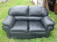 Front view of black faux leather loveseat showing two cushioned seats, padded armrests, and slightly creased seat cushions.