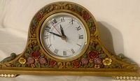 Front view of decorative table top clock showing floral design and clock face.
