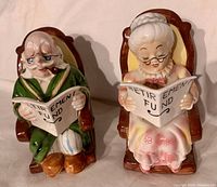 Front view of Grandpa and Grandma ceramic coin banks seated in brown rocking chairs, holding Retirement Fund books.
