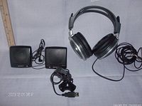 Top-down view showing Sony stereo headphones with coiled cable, two small Sony speakers, and small USB computer microphone with attached stand on a gray surface near a ruler for scale.