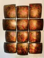 Front view of abstract metal wall art sculpture showing all twelve curved square panels with varied metallic colors and textures.