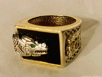 Side angle of the gold color men's ring showing detailed dragon head with emerald green eye and black enamel background.
