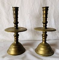 Photo showing front view of the pair of vintage heavy brass candle holders on a white cloth background.
