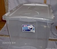 Front view of clear Sterilite plastic storage container with white fold-over lid and black top insert, showing label.