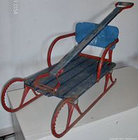 Vintage child's sleigh showing blue wood seat and metal runners with handle for pulling, from a front angle