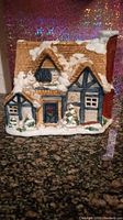 Front view of ceramic snowy cottage figurine showing detailed roof, chimney, and snow accents on roof and around base.