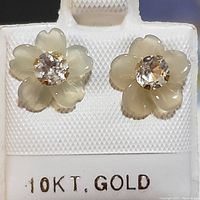 Front view of the pair of 10K yellow gold earrings with flower-shaped carved petals and white topaz centers displayed on holder marked 10KT GOLD.