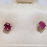 Close-up of two small round ruby stud earrings set in 14K white gold prong settings on display card.