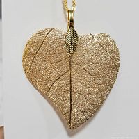 Close-up of the heart-shaped leaf skeleton pendant with detailed veins and texture in a metallic gold finish, hanging from gold chain.