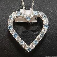 Close-up front view of the heart-shaped pendant with blue and white topaz stones set in sterling silver.