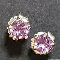 Close-up photo of two round amethyst stones set in sterling silver prong settings against a black background.