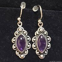 Pair of sterling silver earrings with marquise amethyst stones and decorative silver borders on a black background.