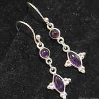 Pair of sterling silver dangle earrings with round and marquise-shaped amethyst stones, displayed on black background.